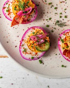 three deviled eggs topped with bacon and vegetables on a white plate, garnished with sprinkles