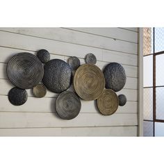 a metal wall hanging on the side of a white building with several circular objects attached to it