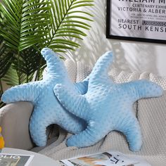 two blue starfish pillows sitting on top of a couch next to a potted plant