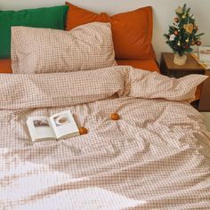 an open book on a bed with orange pillows and plaid comforter, next to a flower pot