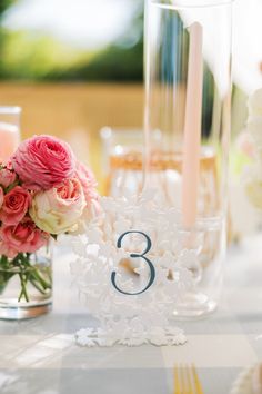 the table is set with pink and white flowers in vases, candles and napkins