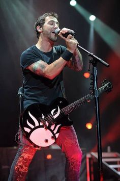 a man on stage singing into a microphone and holding a guitar in front of him