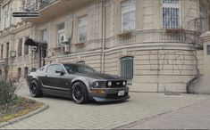 a gray mustang parked in front of a building with graffiti on it's walls