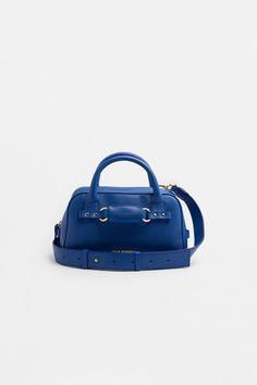 a small blue handbag on a white surface with the handle extended and two gold hardwares