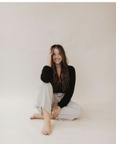 a woman sitting on the floor with her legs crossed and smiling at the camera while wearing white pants