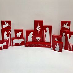 a group of red blocks with white silhouettes of people and animals on them, including a nativity scene