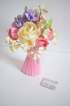 a bouquet of flowers in a pink vase next to a piece of paper with a tag on it