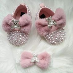 two pairs of pink baby shoes with pearls and bows on the bottom, one has a bow