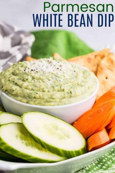 a white bowl filled with dip surrounded by sliced cucumbers and carrots on a plate