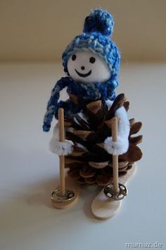 a knitted snowman sitting on top of a pine cone and holding a shovel