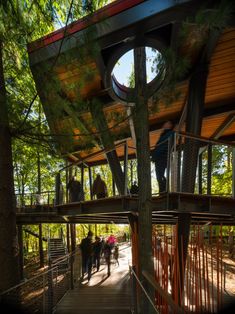 people are walking on a wooden walkway in the woods near a tree house that is surrounded by trees