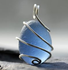 a wire wrapped sea glass pendant sitting on top of a rock