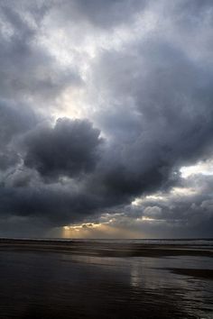 the sky is filled with dark clouds as it sits above the water at low tide