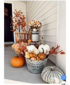 a bucket filled with pumpkins and gourds sitting on the front porch in fall