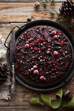 a chocolate cake with cranberries and nuts is on a plate next to pine cones