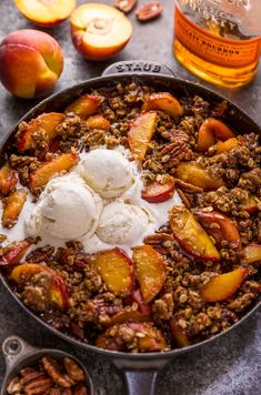 a skillet filled with fruit and ice cream on top of a table next to sliced peaches