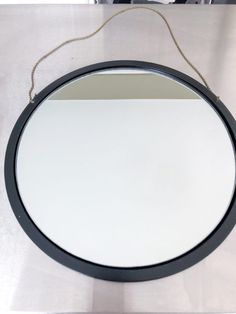 a round mirror hanging on the wall above a counter top with a chain attached to it