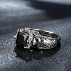 This cute and stunning ring is full of Halloween fun! It's inspired by the "Pumpkin King" - a character and the main protagonist of the famous Halloween film. Crafted in sterling silver, the ring features a princess-cut center stone flanked by two polished skulls on the shoulder of the ring. Glistening stones are set on the shank to add sparkle to the ring. Treat yourself or surprise her with this masterpiece this holiday.Carat Weight: 2.85 ctStone Size: 7*7 mmStone Type: Jeulia® StoneNumber of Stones: 1 Stone Shape: PrincessStone Color: Fancy BlackCarat Weight: 1.89 ctStone Size: 1.5*3,1.5 mmStone Type: Jeulia® StoneNumber of Stones: 44 Stone Shape: Marquise, RoundStone Color: Diamond WhiteWeight: 6.2 gWidth: 10 mmHeight: 9.2 mmThickness: 3.2 mmMaterial: 925 SilverPlating Color: Silver Black Spooky Jewelry For Costume Party, Black Skull Rings As Gift, Black Skull Ring For Halloween, Black Skull Rings For Gift, Halloween Black Skull Ring, Gothic Black Skull Ring For Halloween, Gothic Silver Jewelry For Costume Party, Elegant Jewelry For Halloween Costume Party, Elegant Halloween Jewelry For Costume Party