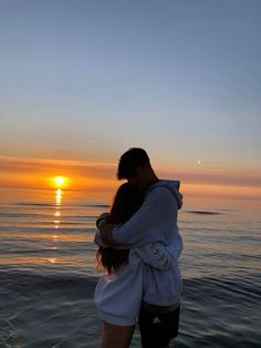 a man and woman embracing in front of the ocean at sunset