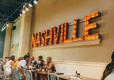 people are sitting at tables in front of the sign for nashville, which is lit up