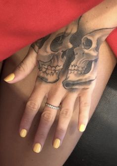 a woman's hand with two skulls on it and yellow nail polishes in front of her