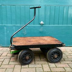 a small wooden cart sitting on top of a brick floor next to a green garage door