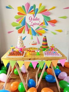 a colorful birthday party with balloons, cake and desserts on a wooden table in front of a white wall