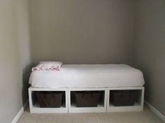 a white bed with three storage bins on the bottom and two brown baskets below it