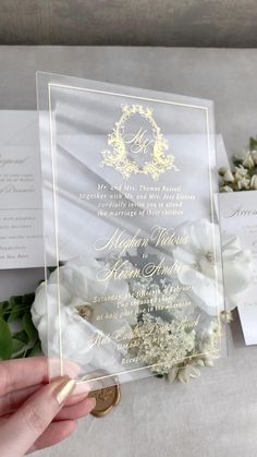 a person holding up a wedding card with flowers in front of it on a table