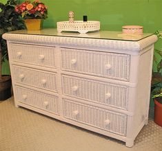 a white wicker dresser sitting in front of a green wall