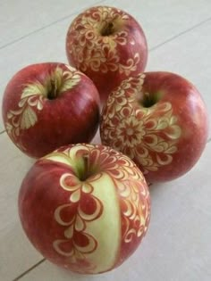 three red apples sitting next to each other on top of a white tile floor with designs painted on them