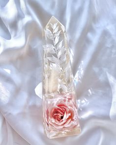 a pink rose in a clear glass vase on a white satin background with leaves and petals