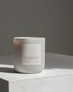 a white candle sitting on top of a table next to a gray wall and floor