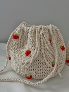 two crocheted bags with strawberries on them sitting on a white cloth surface