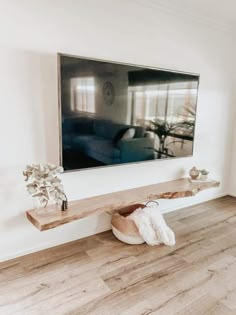 a living room with white walls and wood flooring is featured in this image, there is a large television mounted on the wall