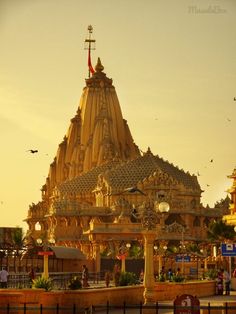 an ornately decorated building in the middle of a town square at sunset with birds flying around