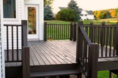 a wooden deck with steps leading up to the front door and grass area behind it