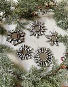 four metal sunbursts hanging on a christmas tree branch with pine cones and berries