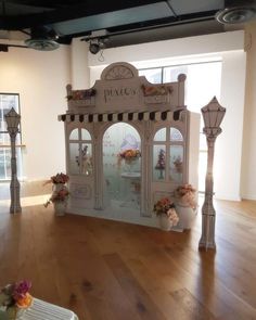 a display case with flowers in it on a wooden floor next to two lamps and windows