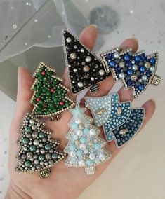 a person is holding five christmas tree brooches in their hands, all decorated with beads