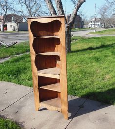 a wooden book shelf sitting on the side of a sidewalk next to a grass field