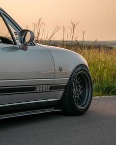 a silver sports car parked on the side of the road near tall grass and weeds