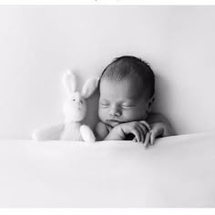 a baby sleeping next to a stuffed animal on top of a white blanket in black and white