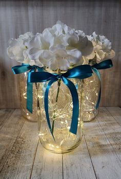 some white flowers are in a glass jar with blue ribbon and lights on the side