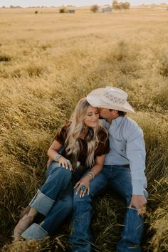 a man and woman sitting on the ground in a field with tall grass looking at each other