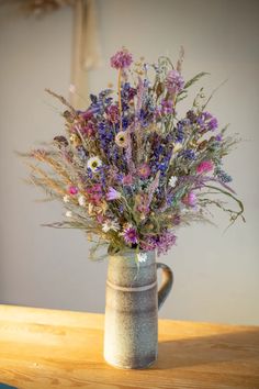 a vase filled with lots of purple flowers on top of a wooden table