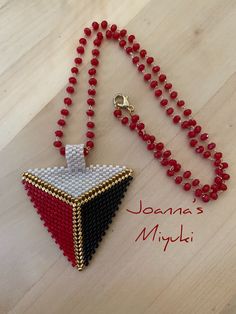 a beaded necklace with a red, white and black triangle pendant on a wooden table