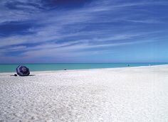 an umbrella is sitting on the beach in front of the blue water and clouds above it