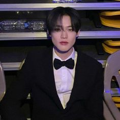 a man wearing a tuxedo and bow tie sitting in front of some chairs