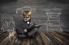 a young boy is sitting on the floor reading a book with stacks of books behind him